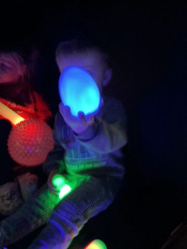 Child holding glowing blue egg-shaped light in dark room.