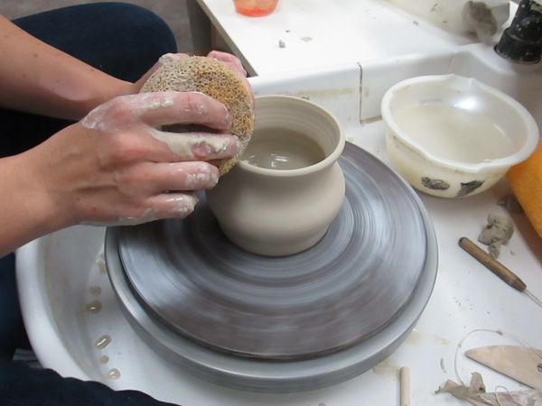 Hands shaping a ceramic pot on a spinning pottery wheel.