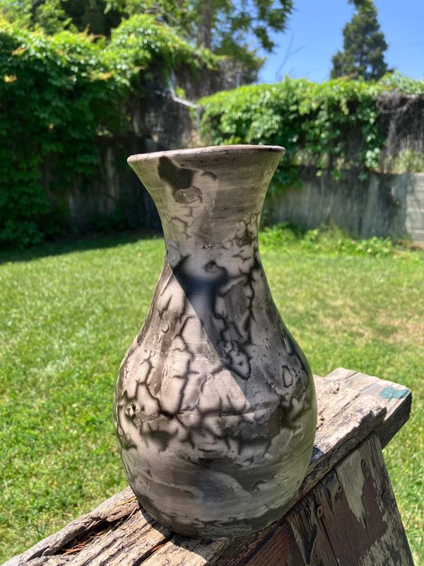 Handcrafted pottery vase with unique marbled patterns on a wooden surface outdoors.