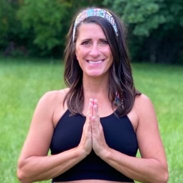 Woman smiling with hands in prayer pose outdoors.