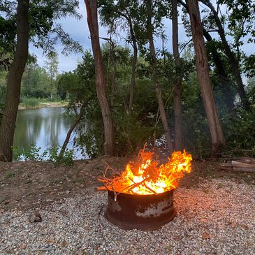 Campfire burning in a metal fire pit by a lake.