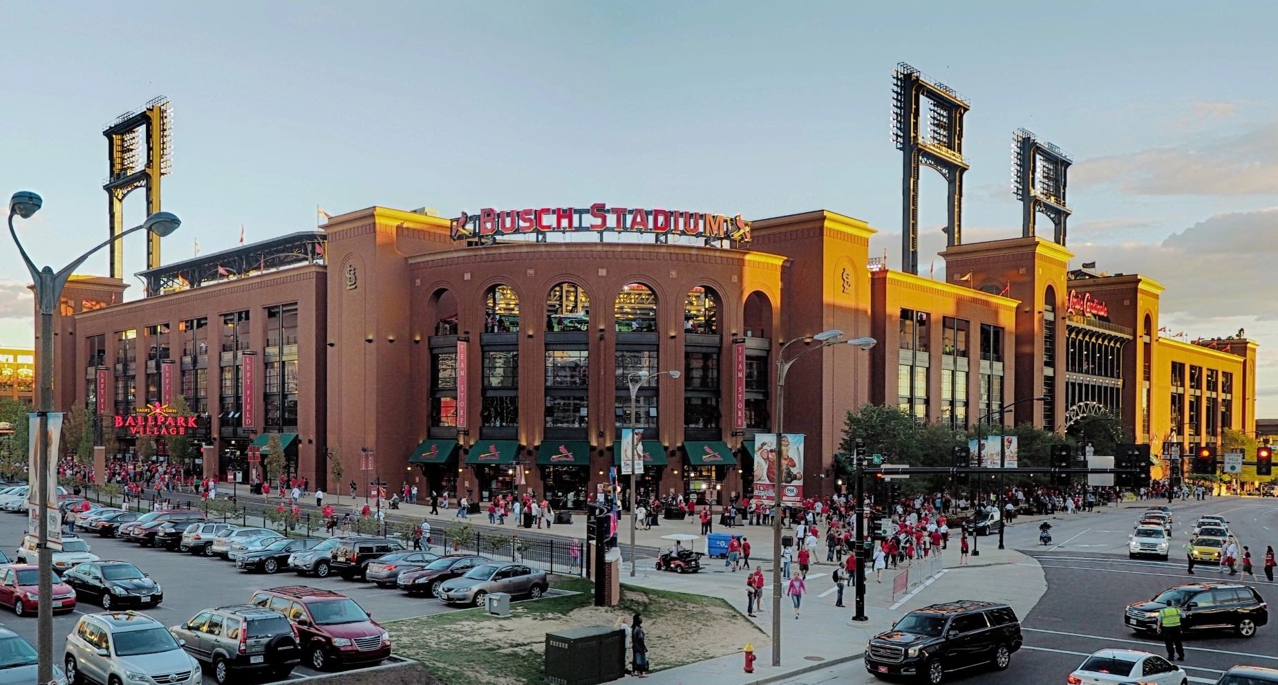 Exterior view of Busch Stadium with people and cars.