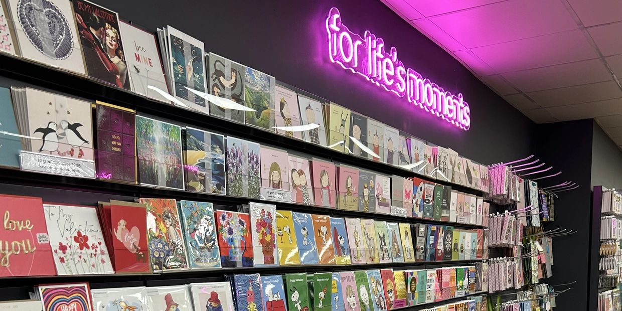 Greeting cards displayed on shelves under neon sign.