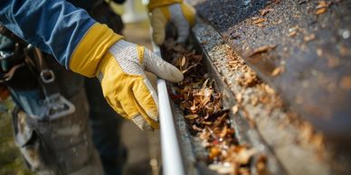 A person wearing gloves cleans leaves from a gutter.