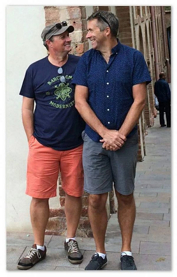 Two men smiling and standing close on a city sidewalk.