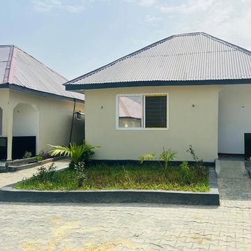 A small, single-story house with a metal roof and a garden in front.
