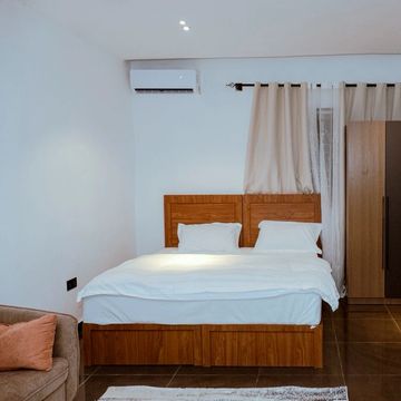 Minimalist bedroom with wooden bed and wardrobe, white walls, and tiled floor.