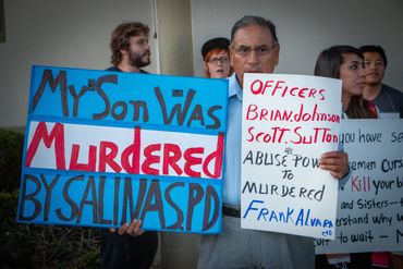 Man holds signs protesting police violence, naming officers involved in his son's murder.