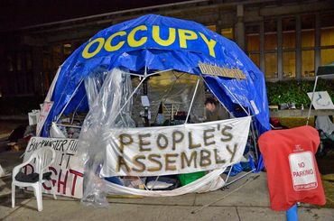 Blue tent with "OCCUPY" and "PEOPLE'S ASSEMBLY" signs at a nighttime protest.