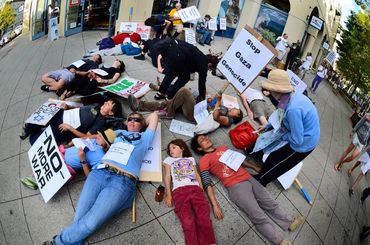 Protesters lying on ground holding signs against Gaza genocide and war.