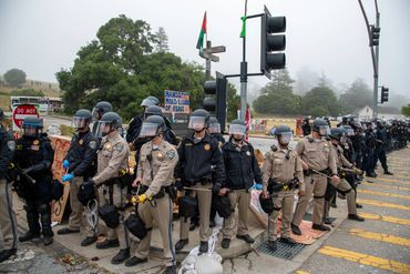 Police officers in riot gear form a line during a protest.
