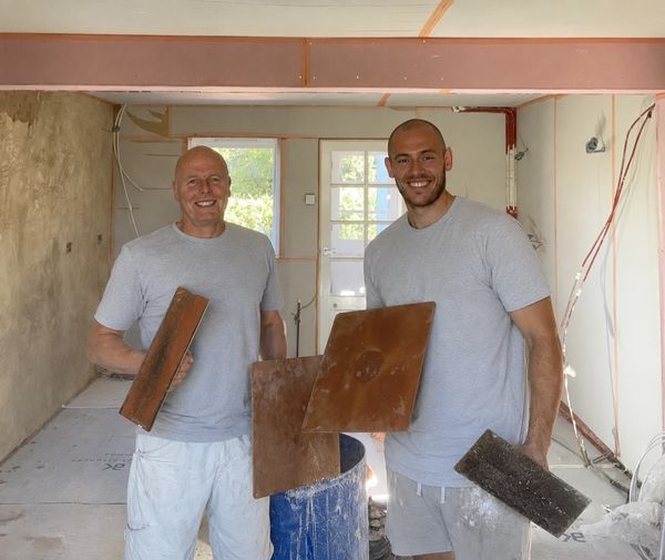 Two men holding construction materials in a room under renovation.