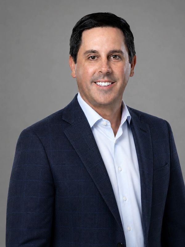 Man in a navy blazer and white shirt smiling at the camera.