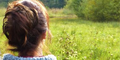 Woman with brown hair looking at a green field on a sunny day.