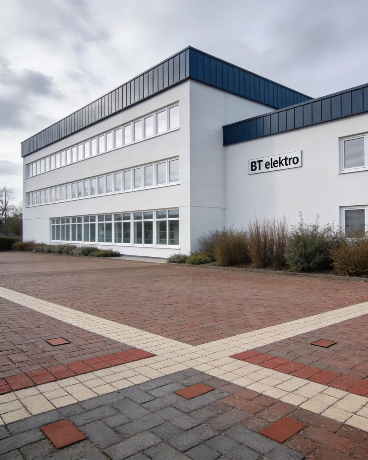 Modern office building with BT elektro signage and patterned brick pavement.