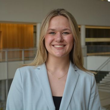 Young woman smiling confidently in a light blue blazer indoors.
