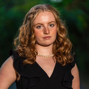 Young woman with curly hair and pearl necklace in black dress.