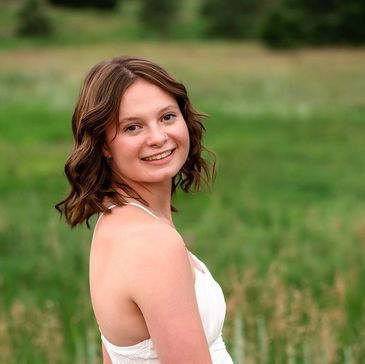 Smiling young woman in white dress outdoors with green field background.