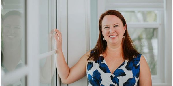 Woman smiling and leaning against a glass wall indoors.