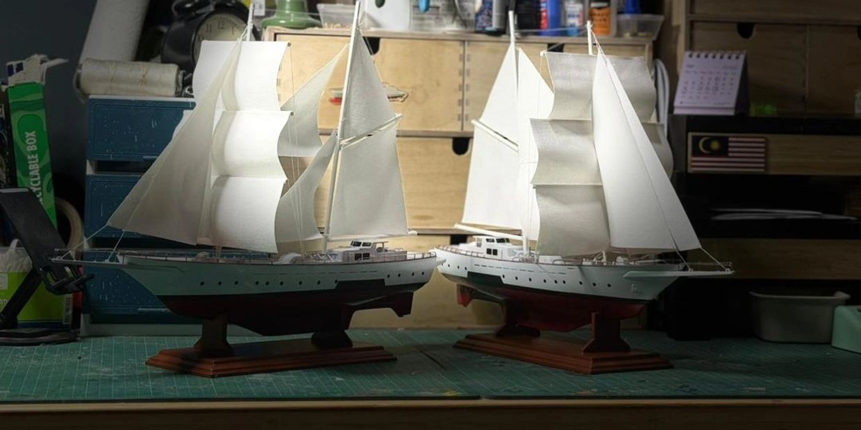 Two detailed model sailboats with white sails on a workbench.