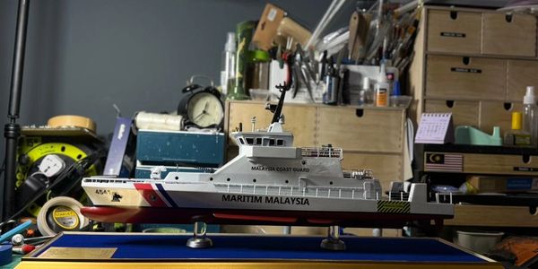 Model of a Malaysian coast guard ship on a desk with tools and storage in the background.