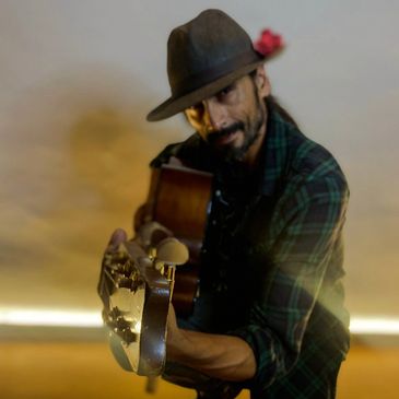 Man with a hat playing guitar, looking at the camera.