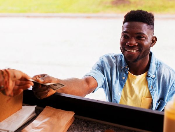 Smiling man pays with cash at a food stand window.
