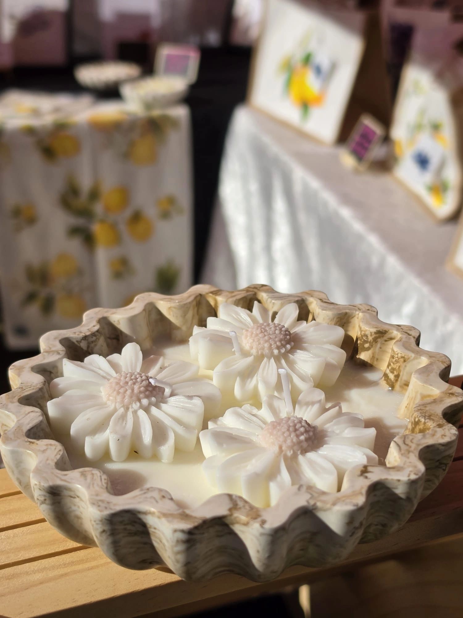 Decorative flower-shaped candles in a carved bowl under warm sunlight.