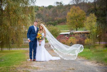 Newlywed couple posing outdoors with a flowing veil and autumn backdrop.