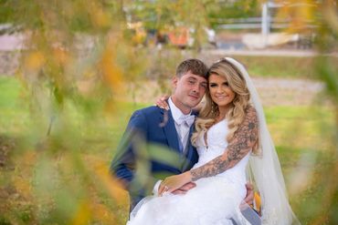 Newlywed couple posing outdoors on their wedding day with autumn foliage.