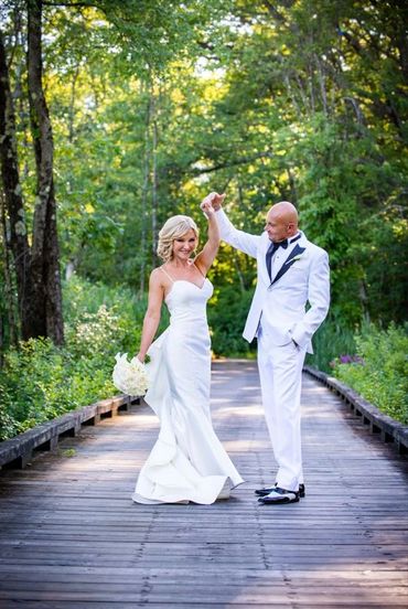 Bride and groom dancing on a wooden pathway in a forested area.