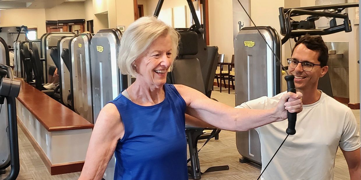 Elderly woman exercising with personal trainer assistance in a gym.
