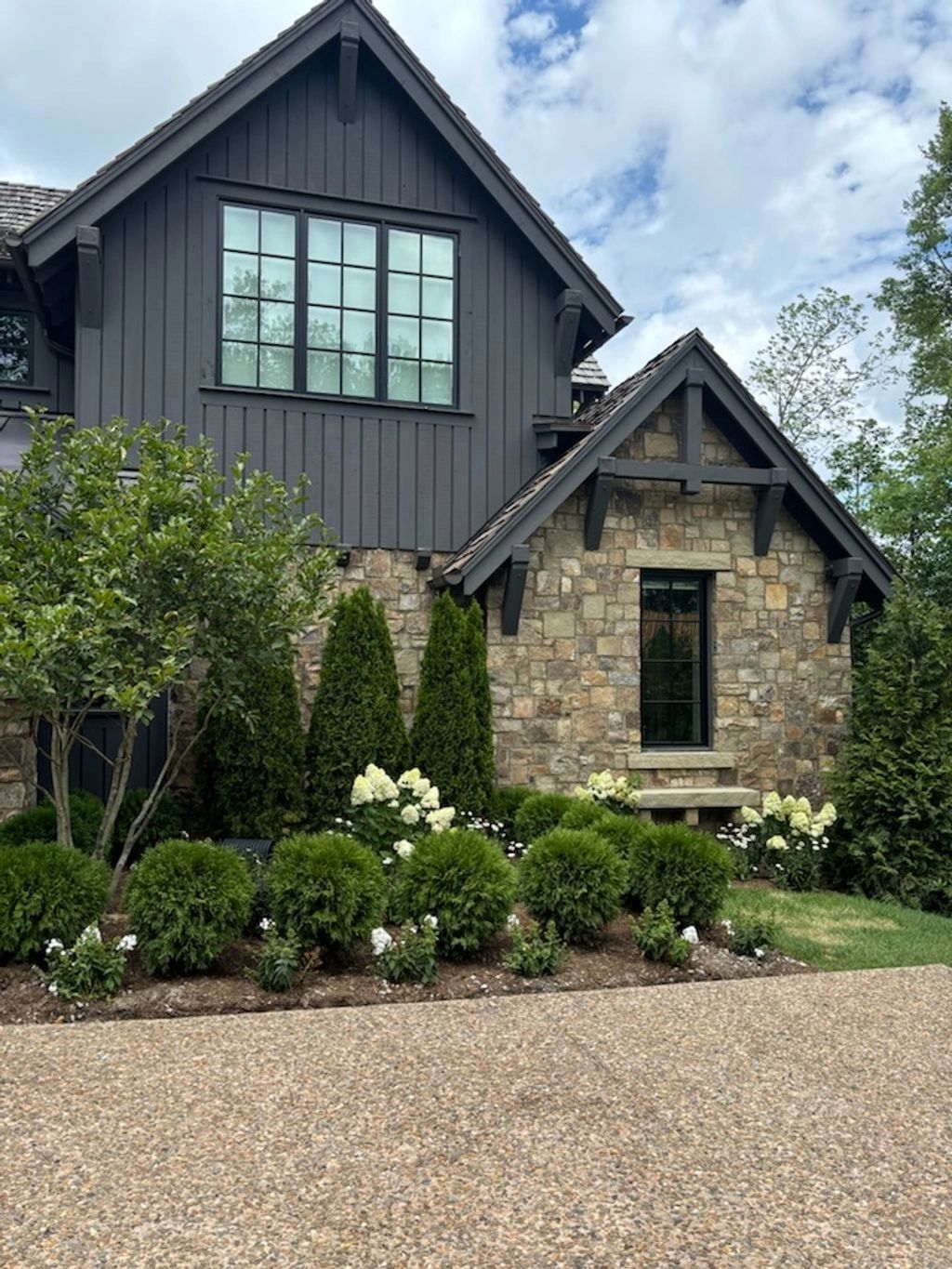 Modern stone and wood house with lush green landscaping and white flowers.