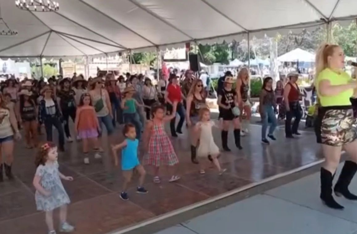 Group dance event under a large tent with kids and adults.