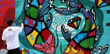 Street artist painting colorful fish mural.