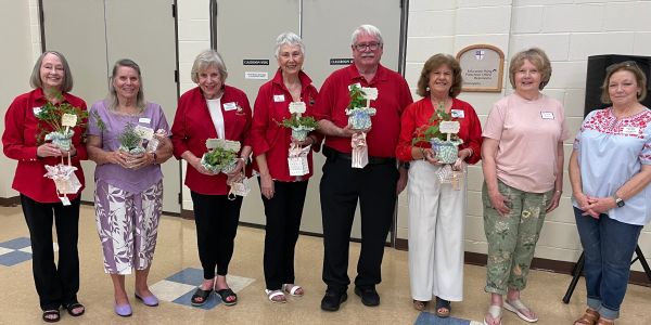 Group of eight adults holding small plant gifts indoors.