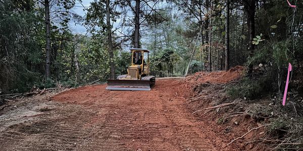Bulldozer leveling a dirt path in a forested area.