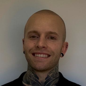 Smiling bald man with neck tattoos and black earrings.