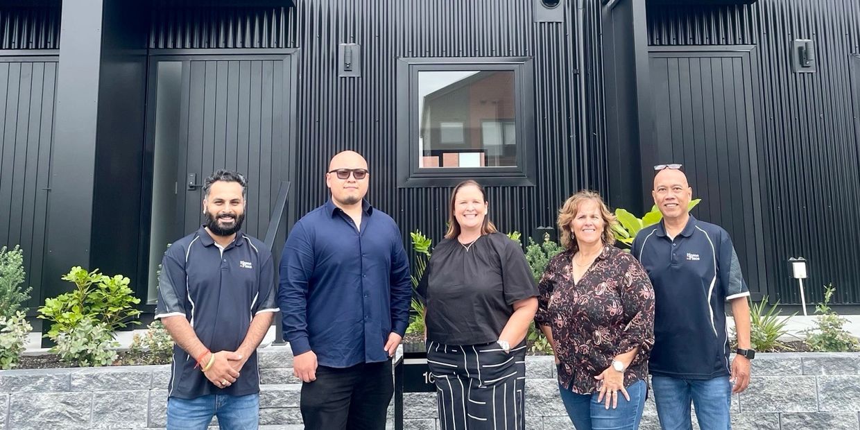 Five people standing in front of a modern black building, smiling at the camera.