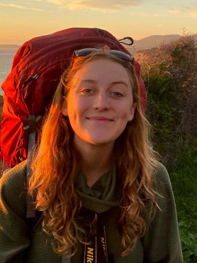 Smiling woman with backpack during sunset.