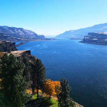 Wide river valley with cliffs and autumn trees under a clear blue sky.