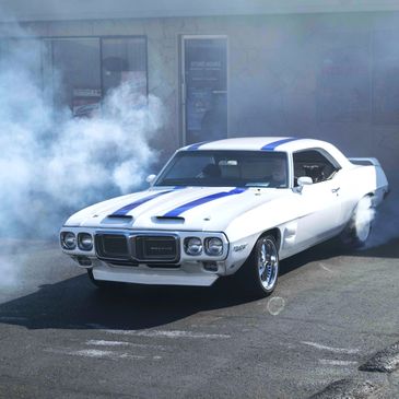 White Pontiac Firebird performing a burnout with smoke surrounding it.