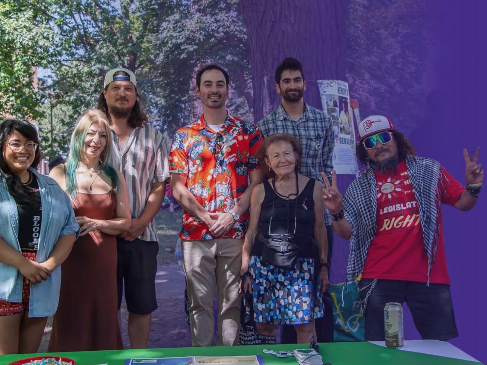 A diverse group of six people smiling outdoors at a table with flyers and buttons.