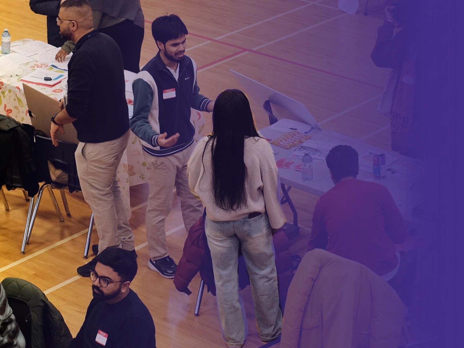 People engaging in conversations at a community event with tables and informational materials.