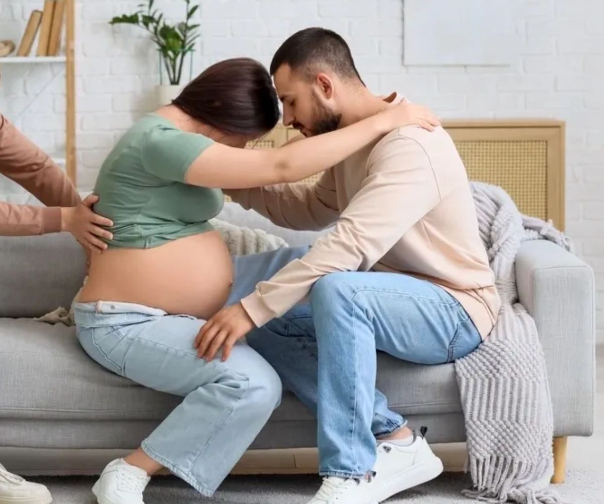 A pregnant woman in labor supported by her partner and Doula on a couch.