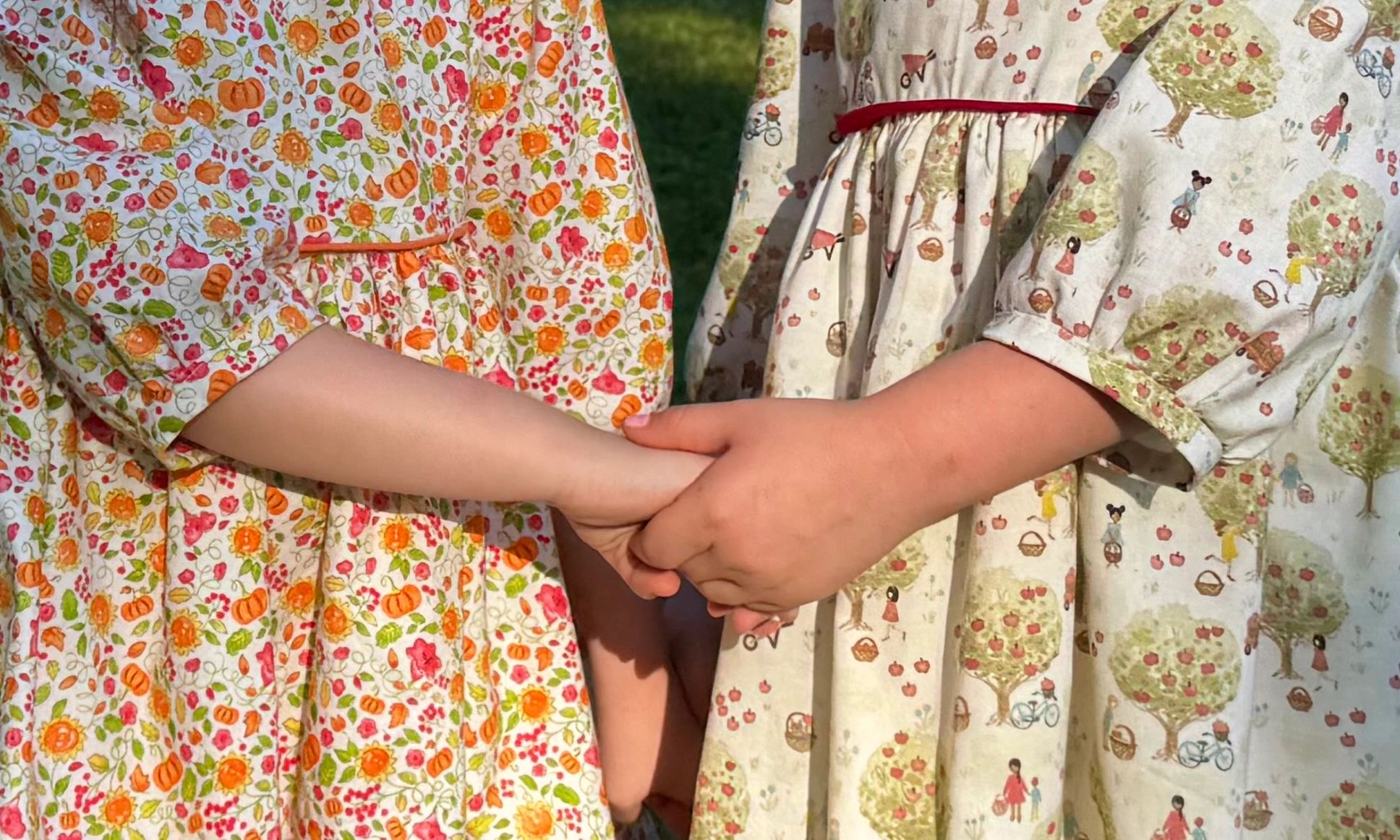 Two girls holding hands in Miss Priss Designs’ handmade fall dresses — perfect for Thanksgiving and special moments.