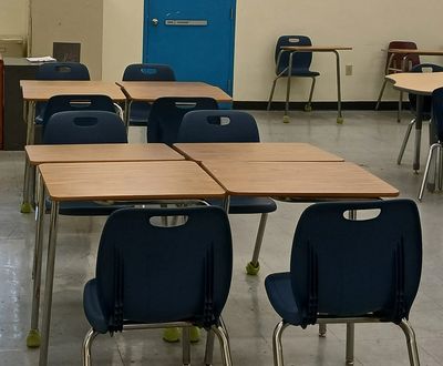 Empty classroom with wooden desks and blue chairs.