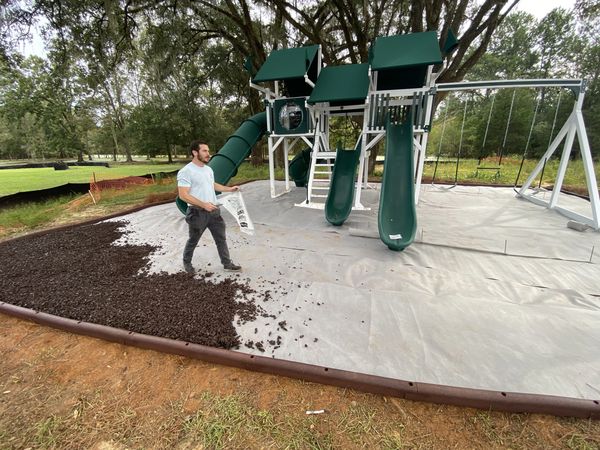 Worker spreading dark rubber mulch for safety area around a playground in Tallahassee Florida