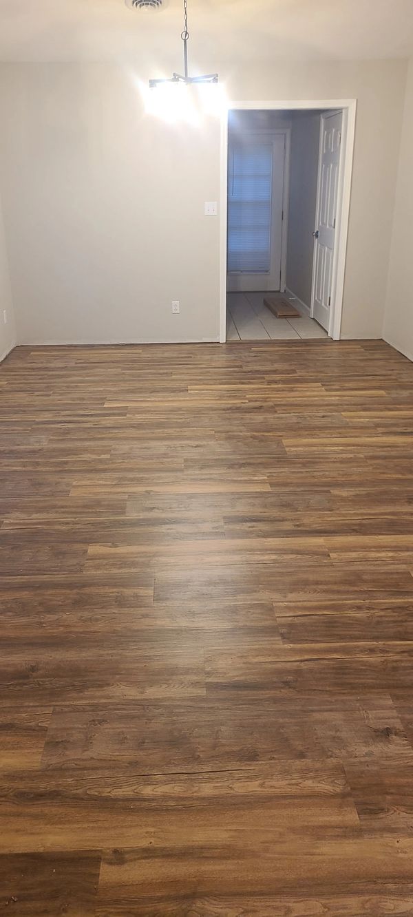 Empty room with wooden flooring and white walls, lit by a ceiling light.
