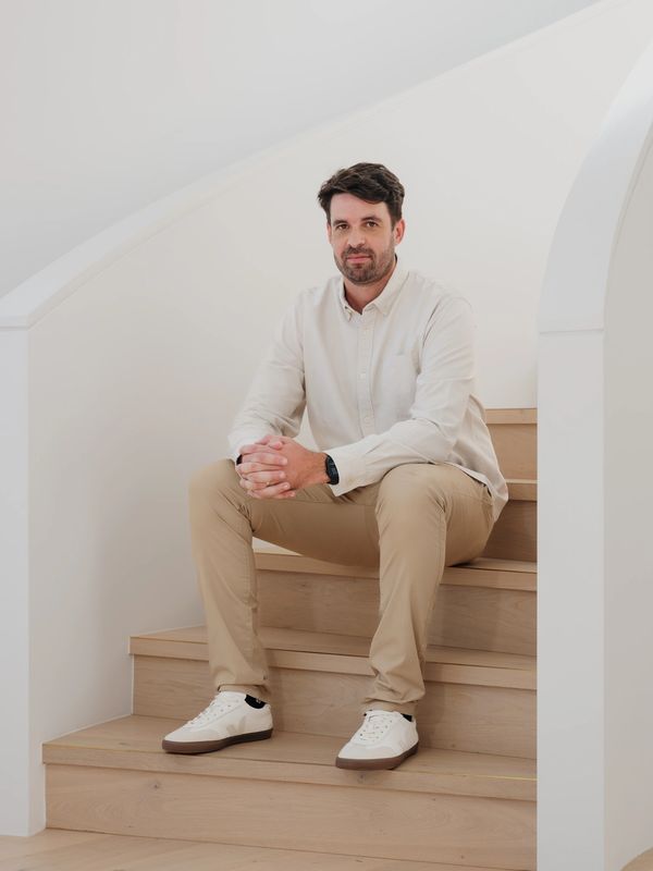 Man sitting on wooden stairs in a modern, minimalistic setting.